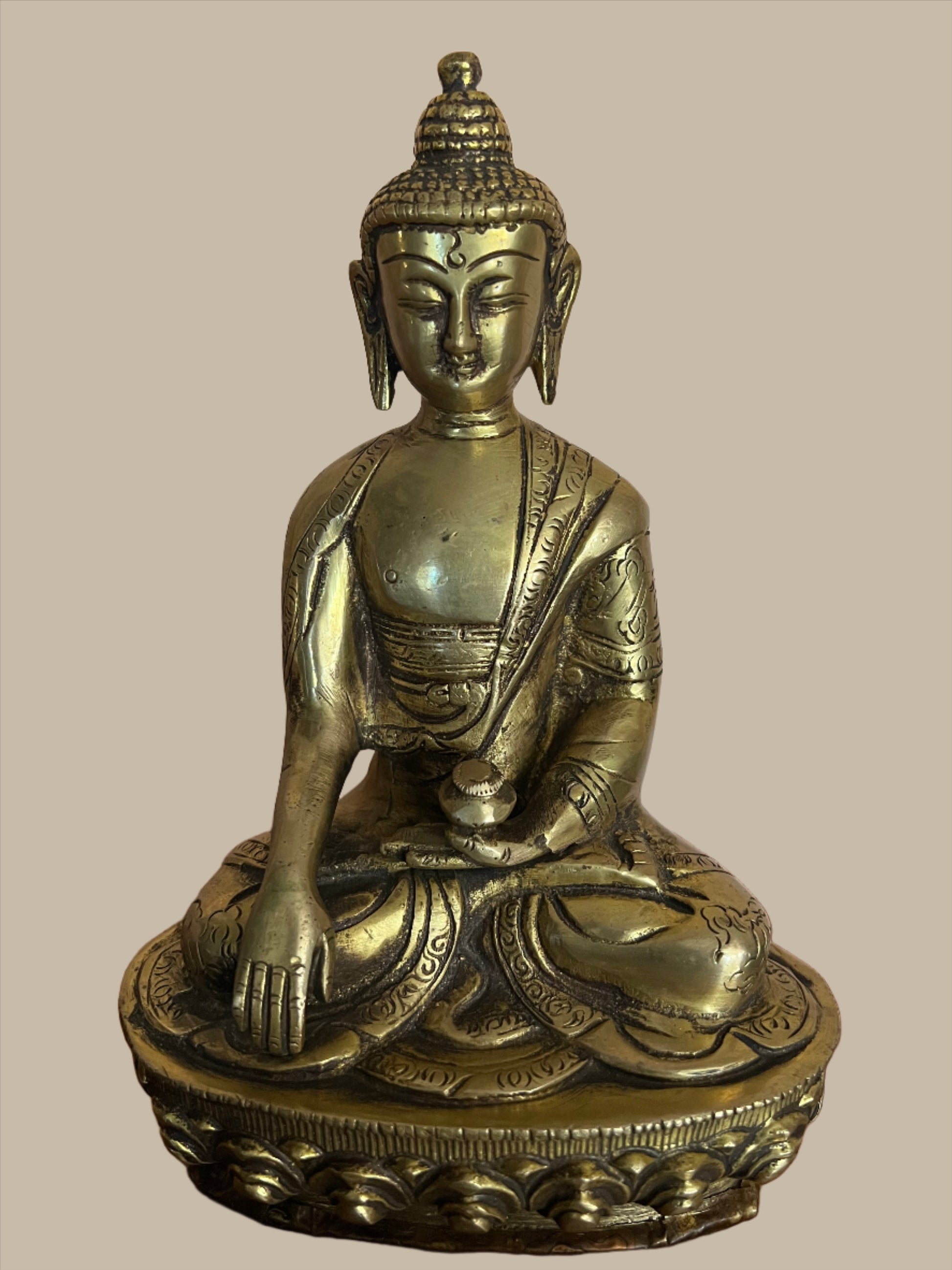 A serene Buddha statue from the Saanskrityam Handicraft Store's Buddha Dharma collection elegantly holds a bowl in its lap. Featuring intricate hair curls, elongated ears, and a flame-like ornament atop its head, this piece enhances any Buddha collection. It stands gracefully on a round, decorated base.