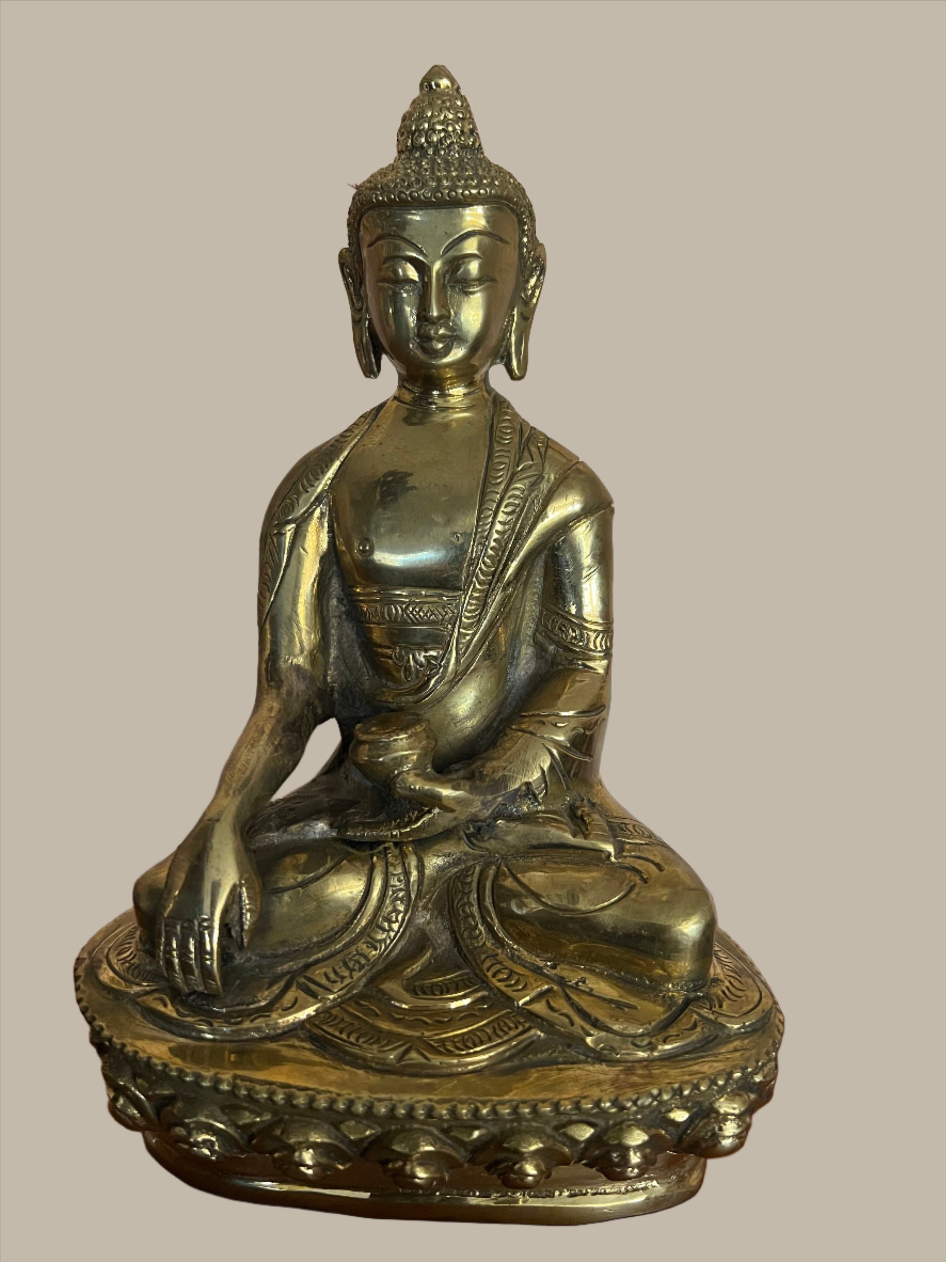 A serene Buddha statue from the Saanskrityam Handicraft Store's Buddha Dharma collection elegantly holds a bowl in its lap. Featuring intricate hair curls, elongated ears, and a flame-like ornament atop its head, this piece enhances any Buddha collection. It stands gracefully on a round, decorated base.