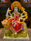Product Name: Durga Marble by Saanskrityam Handicraft Store Description: A vibrant statue of Maa Vaishnodevi, the multi-armed deity perched atop a lion. This intricately designed piece features her adorned with a crown and holding various symbolic objects, while donning a striking red dress accentuated with pink and green accessories. The sculpture is set against an ornate backdrop and rests on a beautifully patterned base, making it an ideal representation for the festive season.