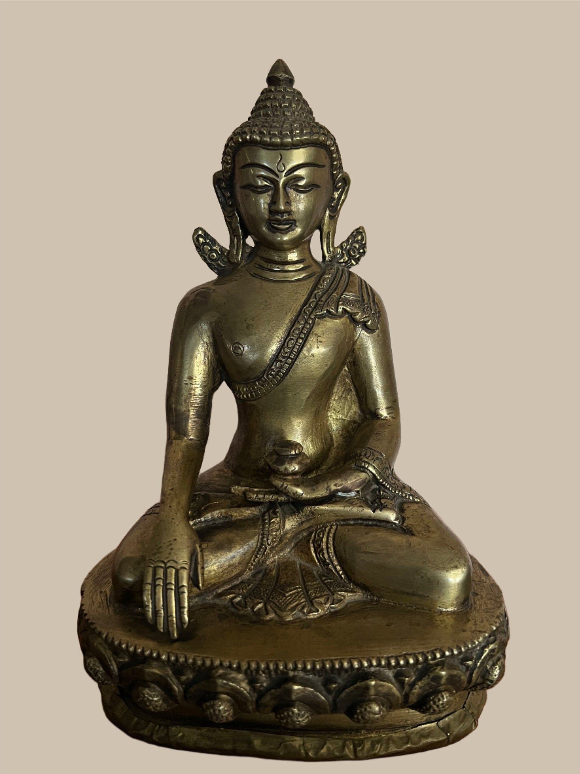 A serene Buddha statue from the Saanskrityam Handicraft Store's Buddha Dharma collection elegantly holds a bowl in its lap. Featuring intricate hair curls, elongated ears, and a flame-like ornament atop its head, this piece enhances any Buddha collection. It stands gracefully on a round, decorated base.
