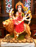 Product Name: Durga Marble by Saanskrityam Handicraft Store Description: A vibrant statue of Maa Vaishnodevi, the multi-armed deity perched atop a lion. This intricately designed piece features her adorned with a crown and holding various symbolic objects, while donning a striking red dress accentuated with pink and green accessories. The sculpture is set against an ornate backdrop and rests on a beautifully patterned base, making it an ideal representation for the festive season.