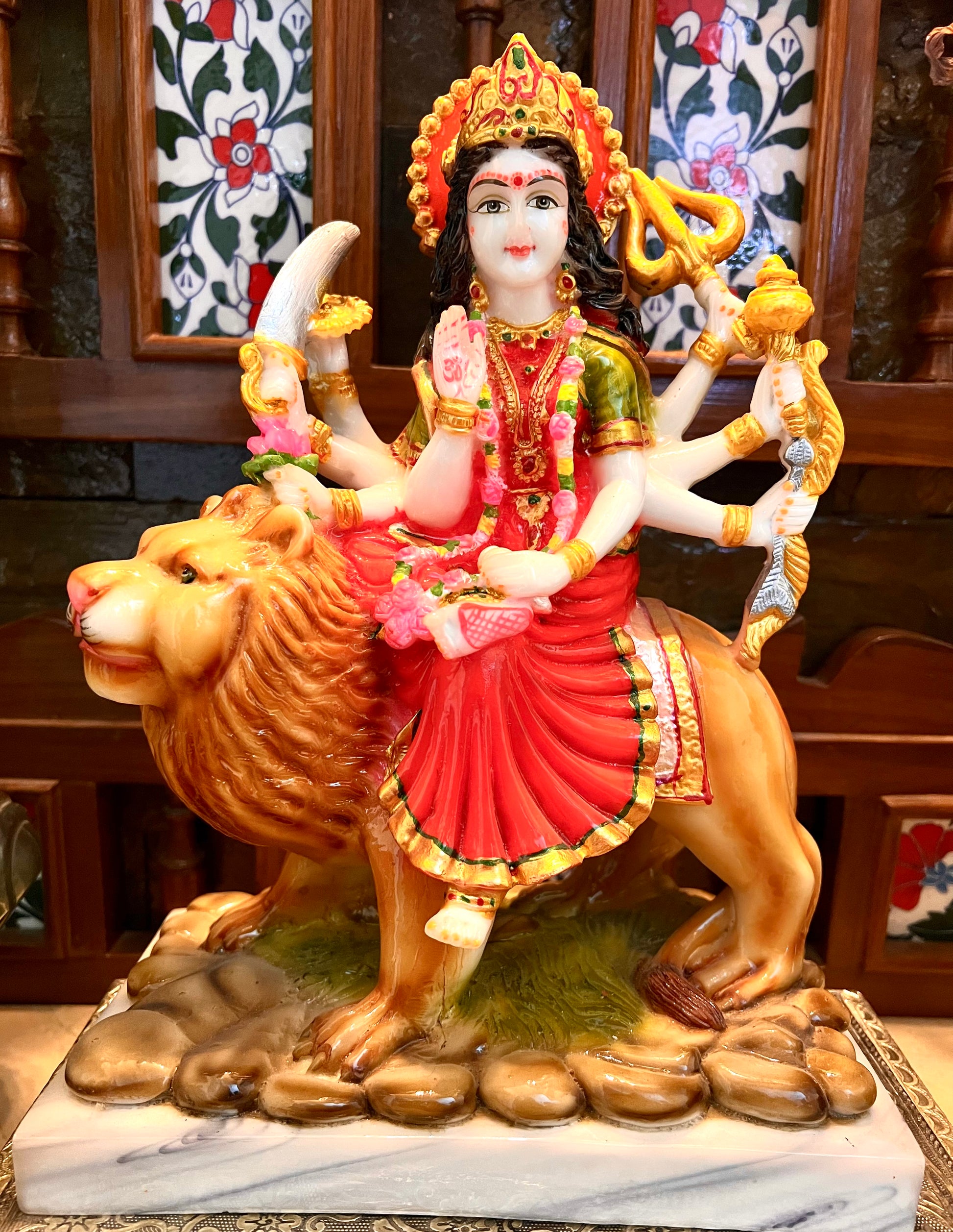 Product Name: Durga Marble by Saanskrityam Handicraft Store Description: A vibrant statue of Maa Vaishnodevi, the multi-armed deity perched atop a lion. This intricately designed piece features her adorned with a crown and holding various symbolic objects, while donning a striking red dress accentuated with pink and green accessories. The sculpture is set against an ornate backdrop and rests on a beautifully patterned base, making it an ideal representation for the festive season.