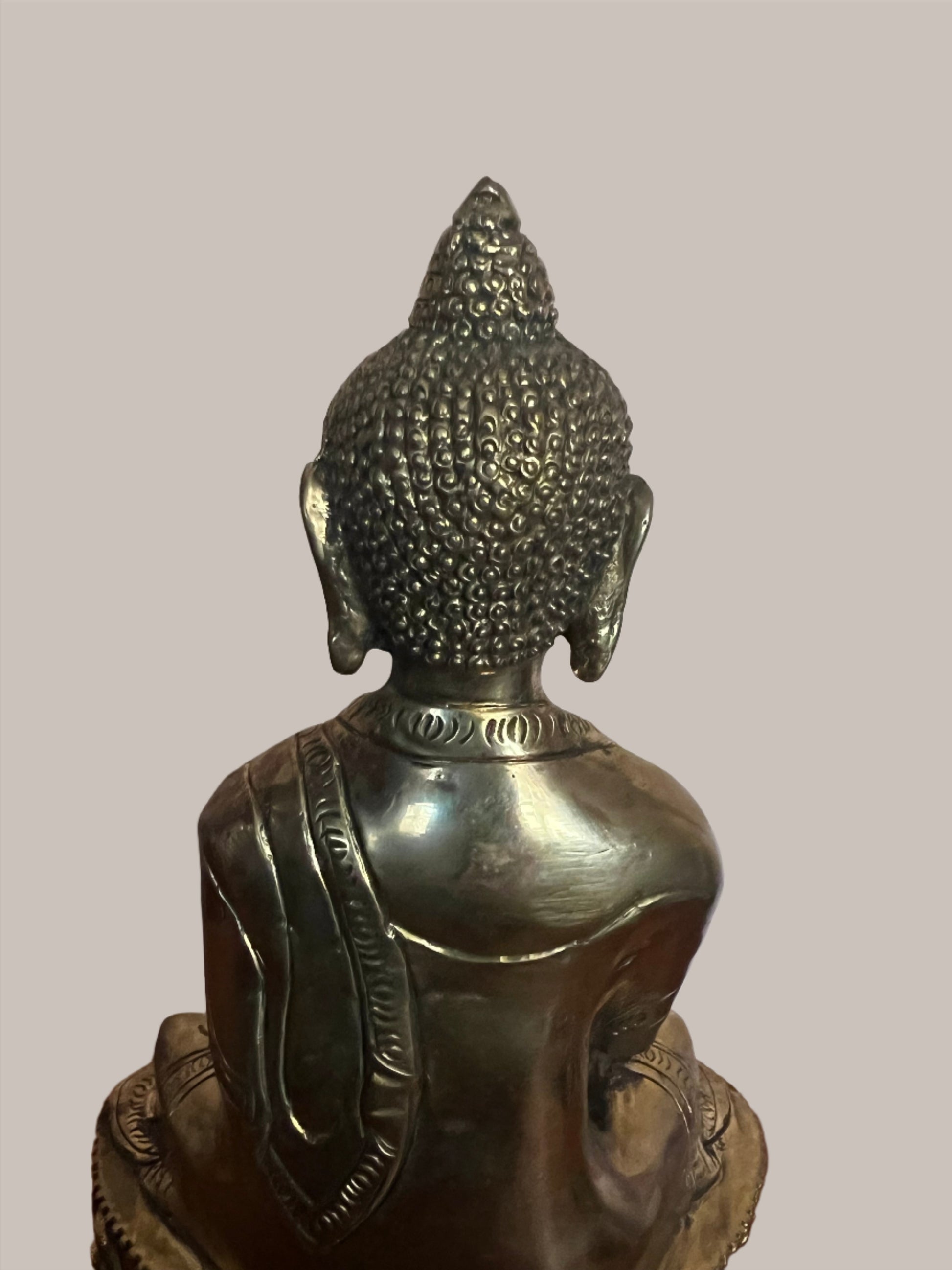 A serene Buddha statue from the Saanskrityam Handicraft Store's Buddha Dharma collection elegantly holds a bowl in its lap. Featuring intricate hair curls, elongated ears, and a flame-like ornament atop its head, this piece enhances any Buddha collection. It stands gracefully on a round, decorated base.
