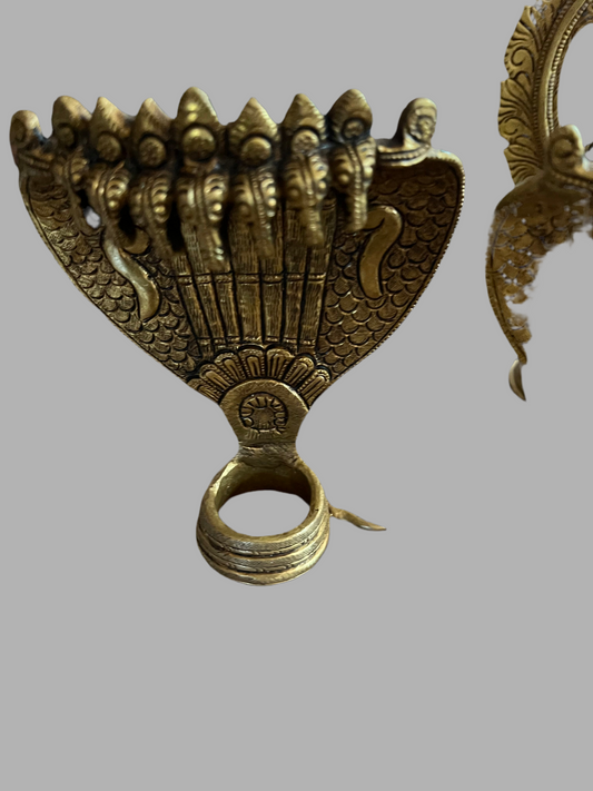 Golden, intricately designed Adisesha Naga bronze sculpture from Saanskrityam Handicraft Store, depicting multiple hooded cobras fanned out like the divine Naga to form a decorative pattern. The plain gray background accentuates the detailed craftsmanship, reminiscent of mythical elegance.