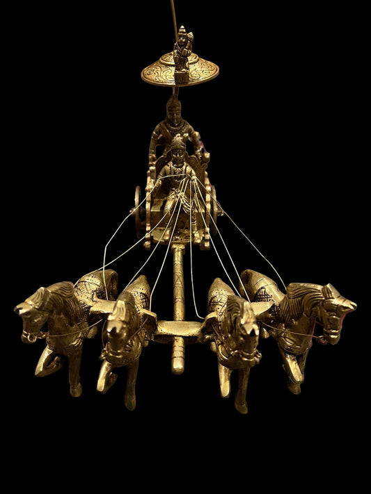 A bronze chariot sculpture named "Krishna and Arjuna / Bhagavad Gita at Kurukshetra," crafted by the Saanskrityam Handicraft Store, depicting four horses with Arjuna and Krishna holding a bow under an umbrella, is elegantly placed on an intricately patterned blue and red rug.