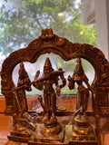 The Kartikeya statue from the Saanskrityam Handicraft Store's Tamilnadu brassware and bronzes collection features a serene depiction of the Hindu God. The brass figure is positioned on a pedestal, holding symbolic items in each hand, while his divine companion—a peacock—stands elegantly beside him, all set against a plain beige background.