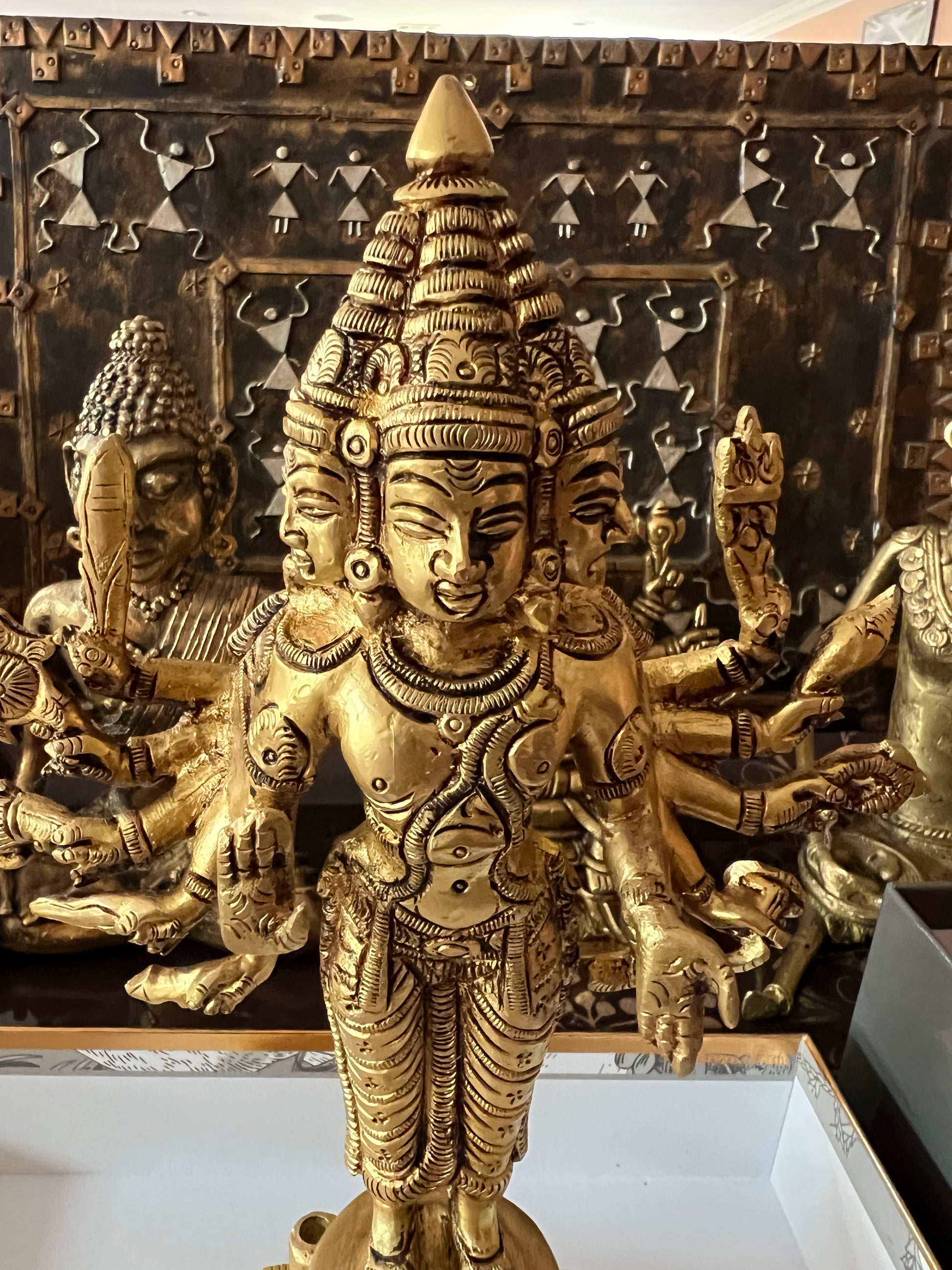 The Kartikeya statue from the Saanskrityam Handicraft Store's Tamilnadu brassware and bronzes collection features a serene depiction of the Hindu God. The brass figure is positioned on a pedestal, holding symbolic items in each hand, while his divine companion—a peacock—stands elegantly beside him, all set against a plain beige background.