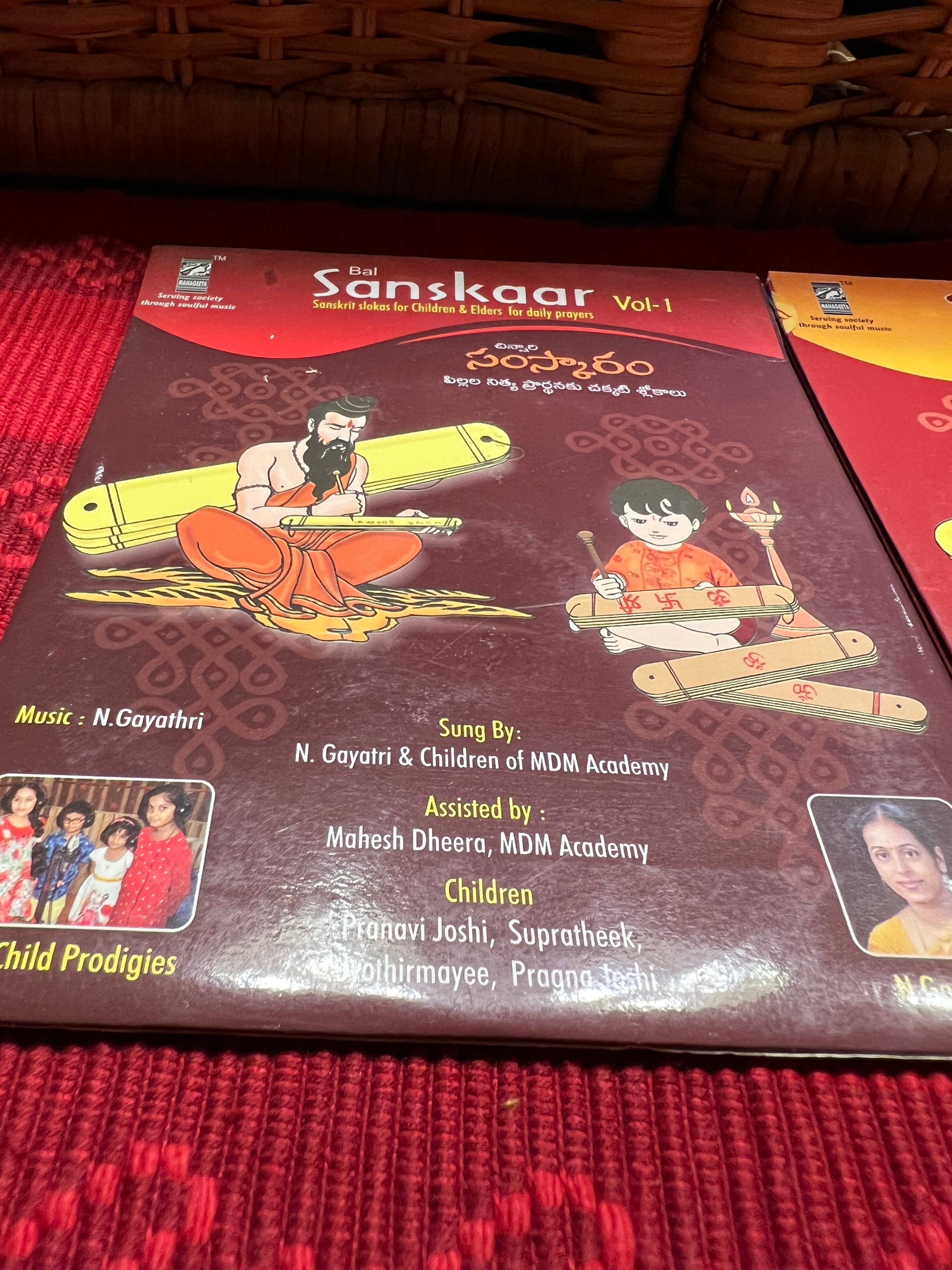 Three packages of the Indian Music Collection incense sticks from Saanskrityam Handicraft Store are arranged on a red fabric. The purple boxes with gold text, featuring an OM symbol and various logos, evoke rich fragrances akin to the soothing notes of Carnatic music.