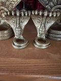 Golden, intricately designed Adisesha Naga bronze sculpture from Saanskrityam Handicraft Store, depicting multiple hooded cobras fanned out like the divine Naga to form a decorative pattern. The plain gray background accentuates the detailed craftsmanship, reminiscent of mythical elegance.