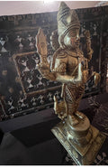 The Kartikeya statue from the Saanskrityam Handicraft Store's Tamilnadu brassware and bronzes collection features a serene depiction of the Hindu God. The brass figure is positioned on a pedestal, holding symbolic items in each hand, while his divine companion—a peacock—stands elegantly beside him, all set against a plain beige background.