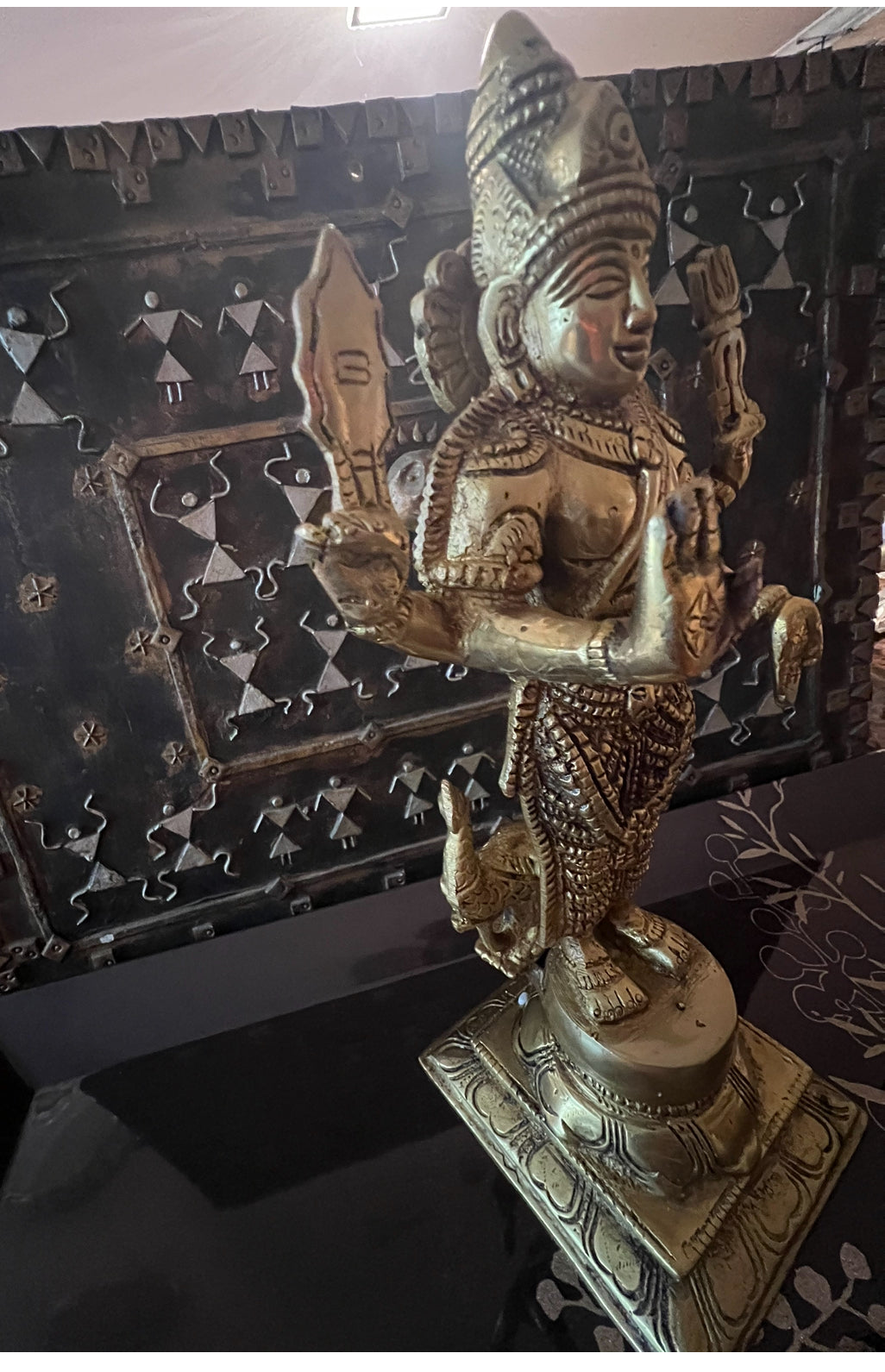 The Kartikeya statue from the Saanskrityam Handicraft Store's Tamilnadu brassware and bronzes collection features a serene depiction of the Hindu God. The brass figure is positioned on a pedestal, holding symbolic items in each hand, while his divine companion—a peacock—stands elegantly beside him, all set against a plain beige background.