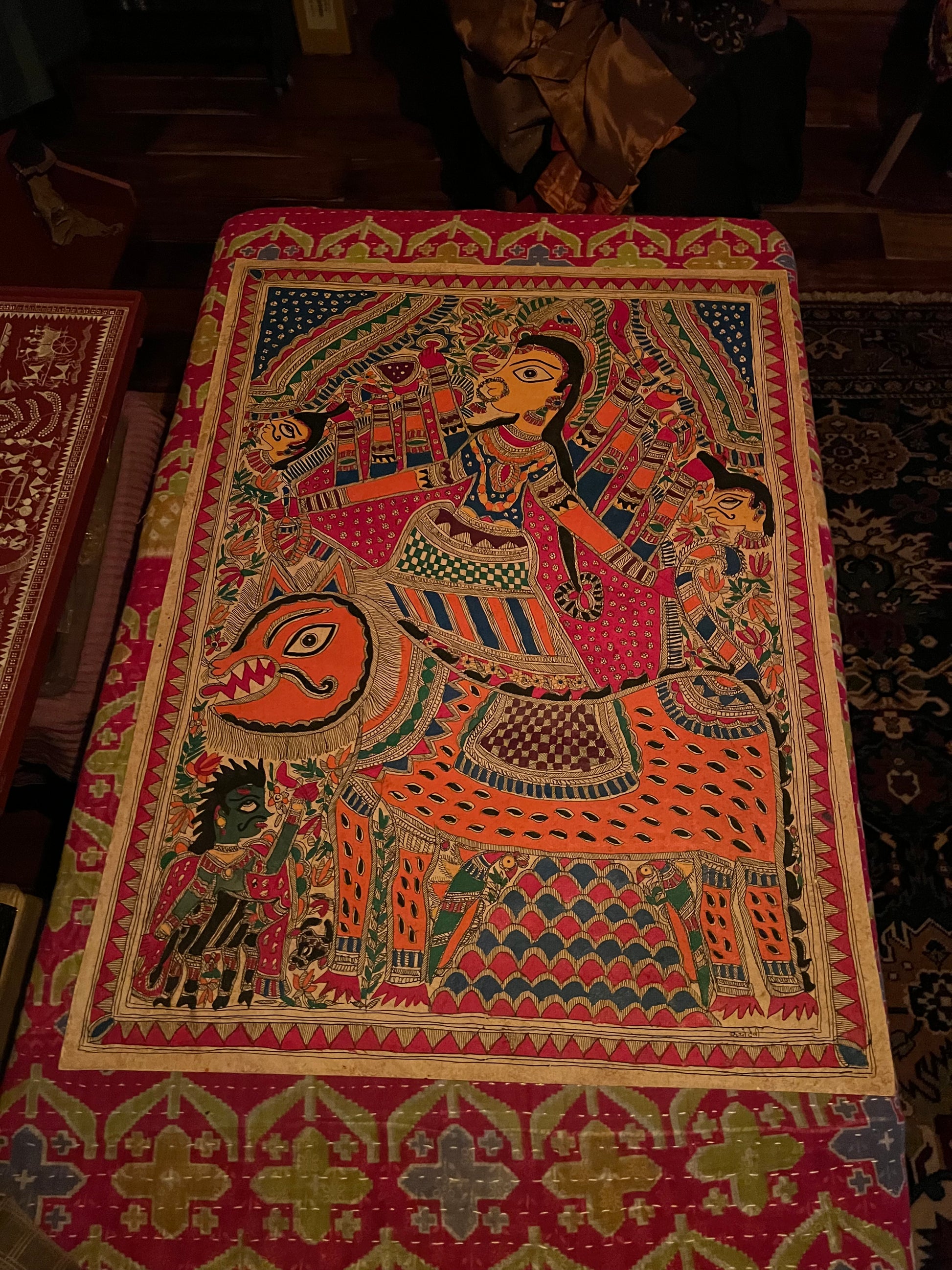 The Mithila or Madhubani style artwork painting from Saanskrityam Handicraft Store beautifully showcases two figures in lively traditional attire, facing each other. One figure is depicted with a yellow face and the other with a blue one, both embellished with intricate patterns and floral motifs. They stand beneath a tree featuring red and green leaves, encapsulating the essence of this folk art style.