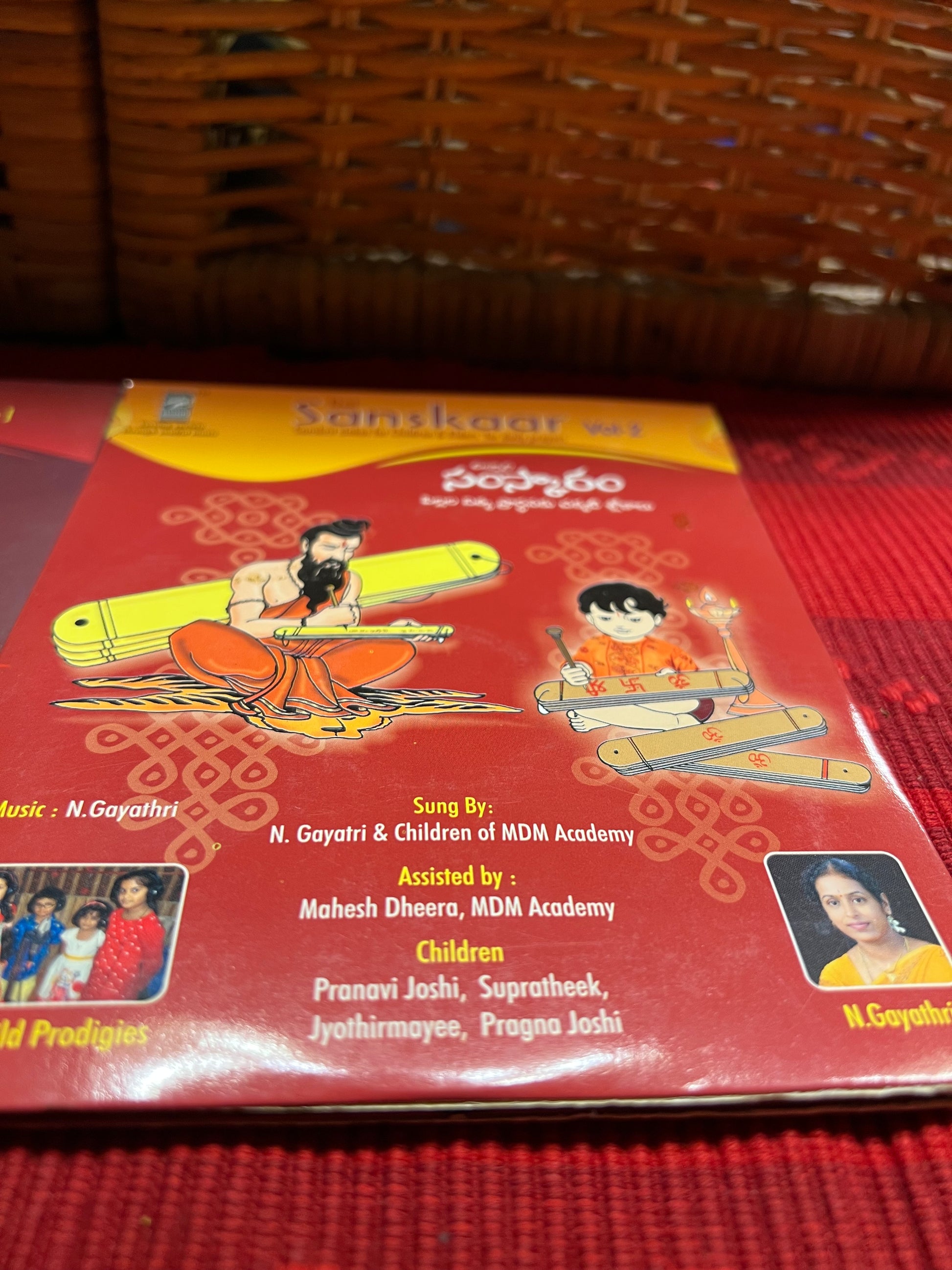 Three packages of the Indian Music Collection incense sticks from Saanskrityam Handicraft Store are arranged on a red fabric. The purple boxes with gold text, featuring an OM symbol and various logos, evoke rich fragrances akin to the soothing notes of Carnatic music.