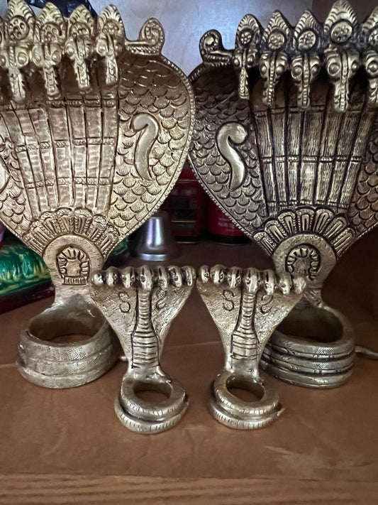 Golden, intricately designed Adisesha Naga bronze sculpture from Saanskrityam Handicraft Store, depicting multiple hooded cobras fanned out like the divine Naga to form a decorative pattern. The plain gray background accentuates the detailed craftsmanship, reminiscent of mythical elegance.