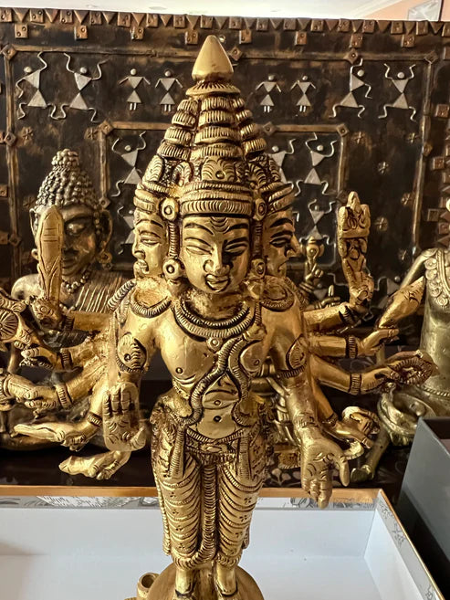 An intricately crafted 10-inch brass statue titled "Arumugam or 6 faced Kartikeya" from Saanskrityam Handicraft Store, showcasing a deity with multiple heads and arms, adorned with traditional attire and jewelry. The backdrop includes additional similar sculptures, hinting at a collection of religious artifacts.