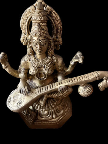 12 inch Saraswathi bronze statue from Saanskrityam Handicraft Store, crafted in Tamilnadu, India, showcases intricate details in the hair, headdress, and facial features. The deity is depicted playing a veena with multiple arms while seated in a serene and divine pose.