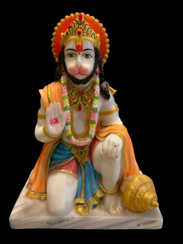 Introducing the 12-inch marble seated Hanumanji from Saanskrityam Handicraft Store. This exquisite statue features a monkey-faced Hindu deity adorned with a colorful headdress and garland, kneeling with one knee elevated. One hand is raised to display a symbol, while the attire showcases a harmonious blend of white, orange, gold, and blue hues. A conch shell is elegantly placed beside it.