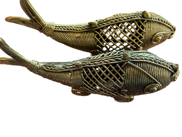 Two intricately designed bronze fish sculptures from Saanskrityam Handicraft Store's Odisha/Orissa collection, crafted in the traditional Dhokra art style of Odisha, showcase detailed weaving patterns and expressive features, positioned side by side.