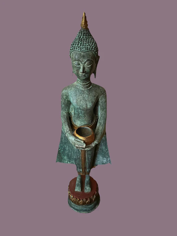 A 22-inch Thai Buddha bronze statue from Saanskrityam Handicraft Store, depicted in a standing pose holding an alms bowl against a plain background. The statue features traditional ornate detailing and exudes a sense of serenity.