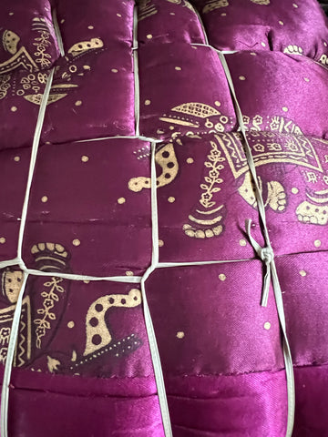 A close-up of the Jaipuri Razai, a cozy queen-size satin comforter by Saanskrityam Handicraft Store, featuring gold elephant designs on a purple background. This exquisite fabric, handmade in Rajasthan, is quilted and secured with white ties.