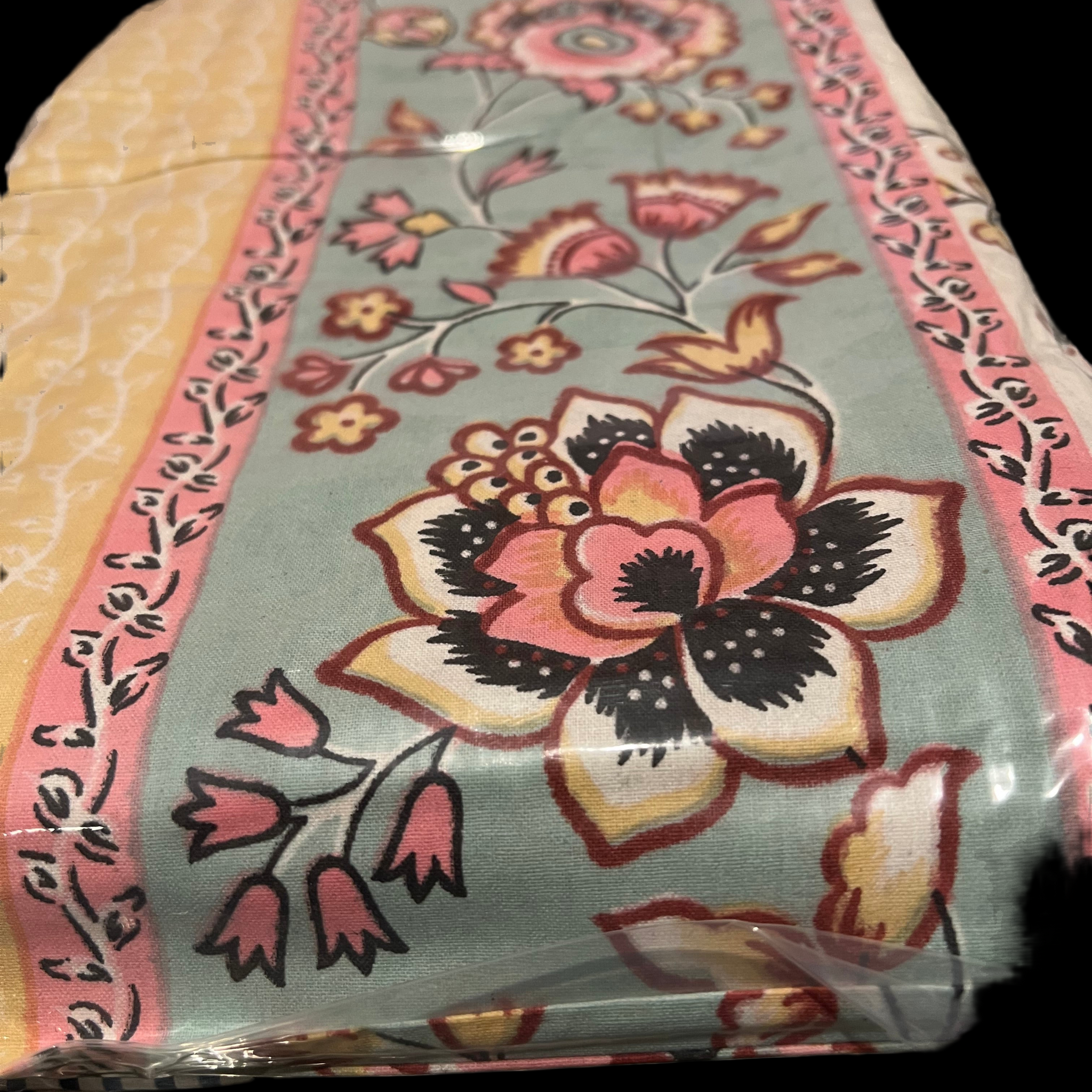 A carefully folded Indian cotton bedspread from the Saanskrityam Handicraft Store, decorated with a striking floral design featuring large blooms and smaller flowers in pink, yellow, and black on a light blue background. The piece is framed by a pink and yellow pattern inspired by traditional Indian motifs, and it comes neatly wrapped in clear plastic as part of the Saanskrityam gifts' Indian cotton collection. This versatile set includes two matching pillowcases, suitable for a queen or full-size bed.