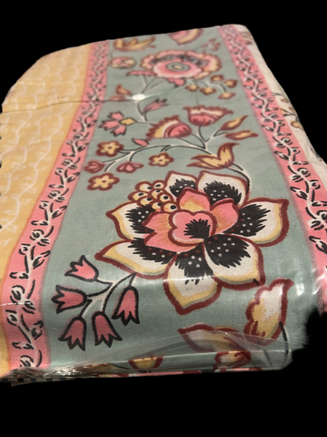 A carefully folded Indian cotton bedspread from the Saanskrityam Handicraft Store, decorated with a striking floral design featuring large blooms and smaller flowers in pink, yellow, and black on a light blue background. The piece is framed by a pink and yellow pattern inspired by traditional Indian motifs, and it comes neatly wrapped in clear plastic as part of the Saanskrityam gifts' Indian cotton collection. This versatile set includes two matching pillowcases, suitable for a queen or full-size bed.