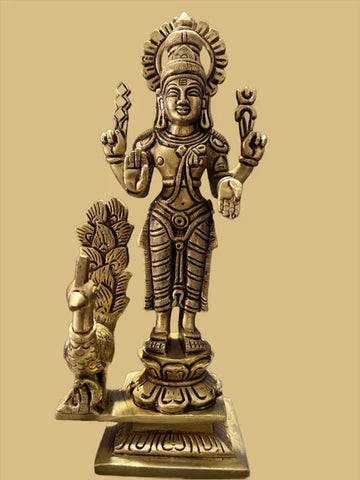 Introducing the "8 inch Kartikeya bronze with peacock and weapons" from Saanskrityam Handicraft Store. This exquisite bronze statue features a standing deity with intricate detailing, clutching symbolic objects in each hand. The deity is embellished with traditional ornaments and is accompanied by a peacock on the left side, all set against a plain beige background.