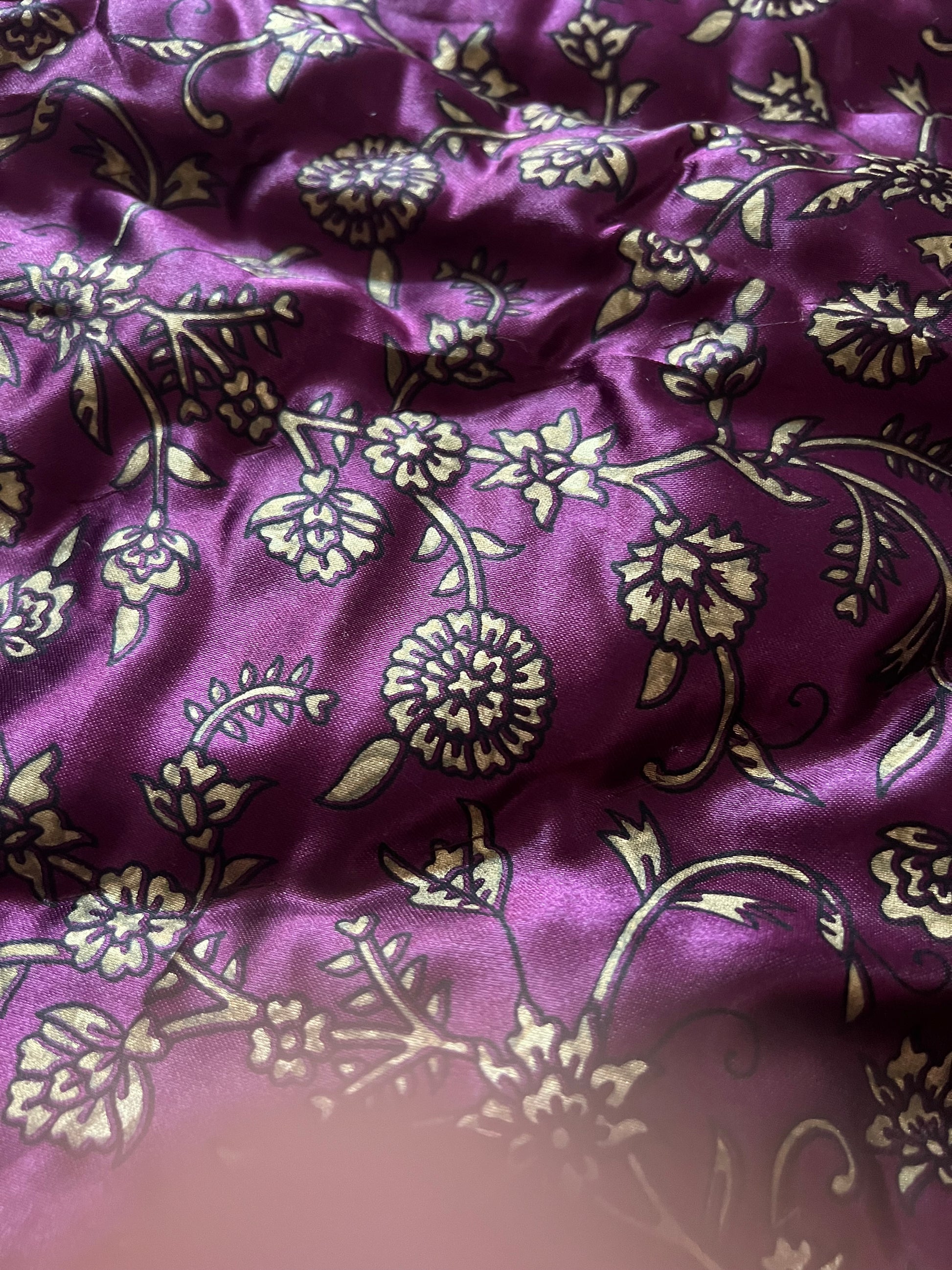 A close-up of the Jaipuri Razai, a cozy queen-size satin comforter by Saanskrityam Handicraft Store, featuring gold elephant designs on a purple background. This exquisite fabric, handmade in Rajasthan, is quilted and secured with white ties.