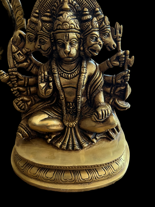 A brass figurine from the Marble Collection by Saanskrityam Handicraft Store, featuring a multi-headed, multi-armed depiction inspired by the esteemed Hanuman statue. The deity is seated in a meditative pose, intricately holding various symbolic objects. This handmade piece rests on an ornate circular base against a black background.