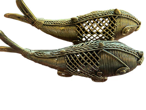 A pair of fish from Saanskrityam Handicraft Store, featuring intricately designed bronze sculptures with woven patterns and detailed features, are positioned side by side against a plain background.