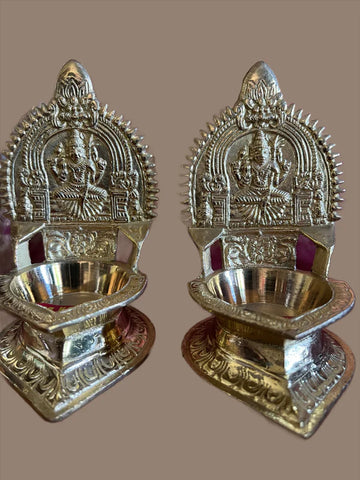 A pair of small-medium Kamakshi lamps from Saanskrityam Handicraft Store, intricately designed with ornate carvings and a high back adorned with a deity figure, polished and set against a plain background.