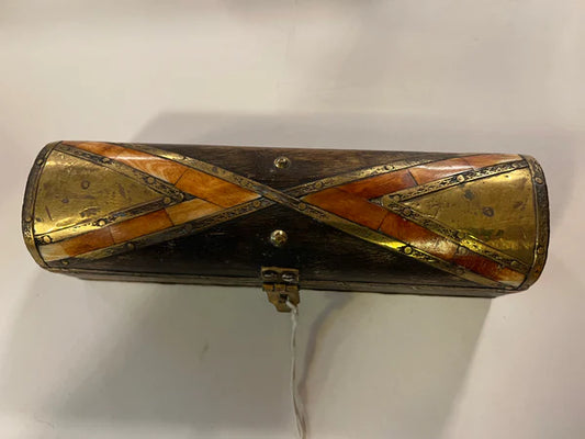 A brass and bone work box from the Saanskrityam Handicraft Store, featuring a cylindrical wooden design with ornate brass and orange inlay forming an X pattern on the lid. The box includes a small metal latch for closure and is showcased against a light background.