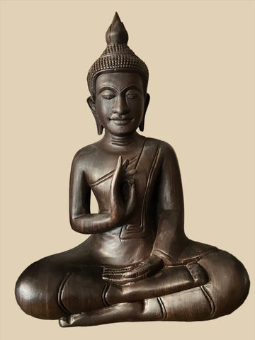 A Cambodian dark wood seated Buddha from Saanskrityam Handicraft Store, featuring a meditative pose with one hand raised and the other resting on the knee. The statue showcases intricate details on the robe and headpiece, set against a plain background.