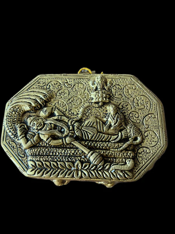 The Dasavataaram bronze box from Saanskrityam Handicraft Store features an ornate rectangular design with an intricate embossed scene, highlighting a reclining figure beneath a canopy and stylized floral patterns, set against a black background.