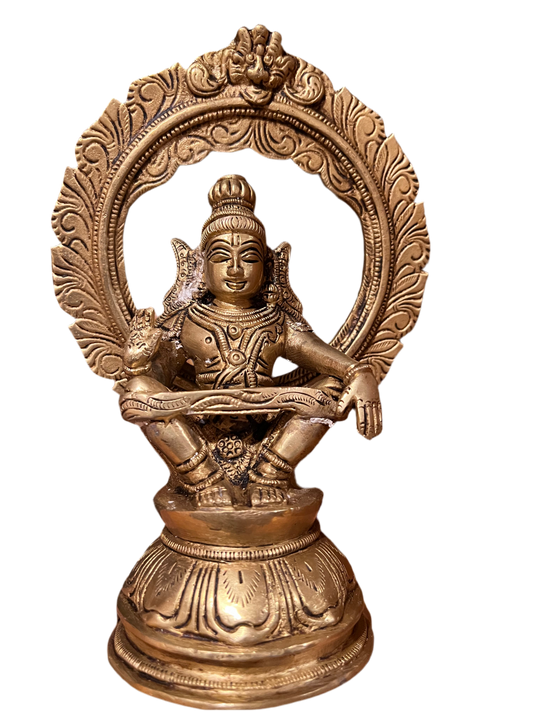 A 7-inch "Sri Ayyappa bronze with arch" statue from Saanskrityam Handicraft Store is displayed on a wooden shelf. The deity is depicted in a meditative pose, enclosed within an ornate bronze arch, with intricate details adorning both the figure and base. Other decorative objects can be partially seen in the background.