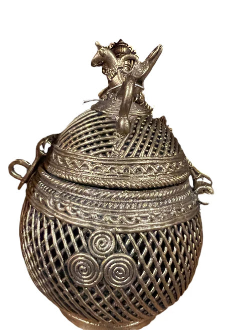 Hen box by Saanskrityam Handicraft Store features an ornate metal design with intricate lattice work and swirling patterns. It is adorned with a decorative top displaying a figure riding an animal, showcasing detailed craftsmanship and traditional artistic elements.