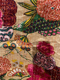 Close-up of the colorful cotton Indian bohemian patchwork quilt from Saanskrityam Handicraft Store, featuring vibrant floral patterns in shades of pink, orange, and green set against a blue background. This king-size design showcases various flowers and leaves with white stitching running vertically across the fabric.