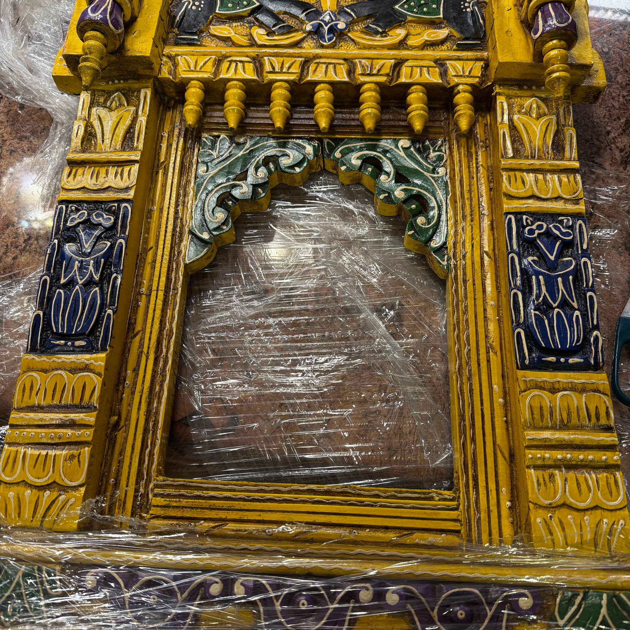 The Saanskrityam Handicraft Store offers a yellow, black, purple, and green ornate wood jharokha (24x17 inches), featuring intricate carvings, vibrant patterns, decorative pillars, and a small arch.