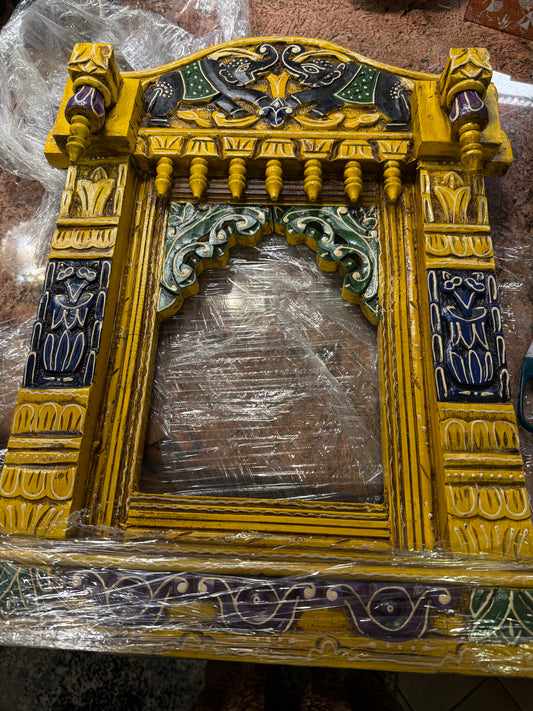 The Saanskrityam Handicraft Store offers a yellow, black, purple, and green ornate wood jharokha (24x17 inches), featuring intricate carvings, vibrant patterns, decorative pillars, and a small arch.