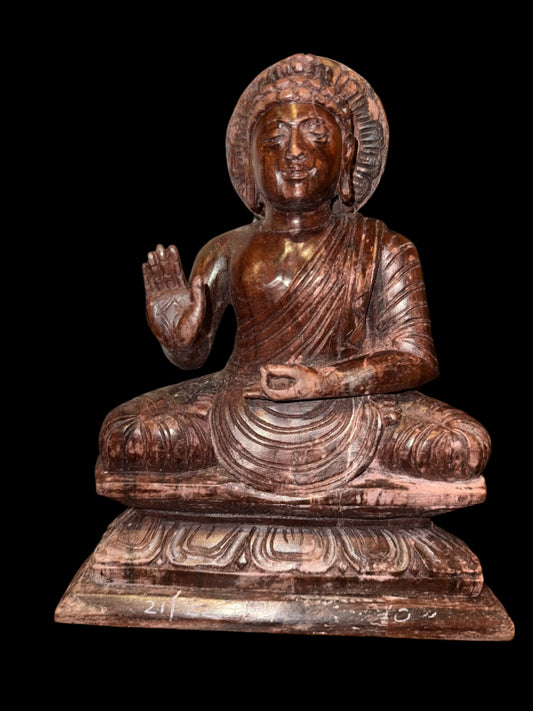 Introducing the 11-inch Buddha crafted from mixed wood grain by Saanskrityam Handicraft Store. This statue showcases a seated Buddha with an ancient aesthetic that enriches its serene expression. The intricate carvings, with one hand raised in a blessing gesture, are elegantly set against a black background.