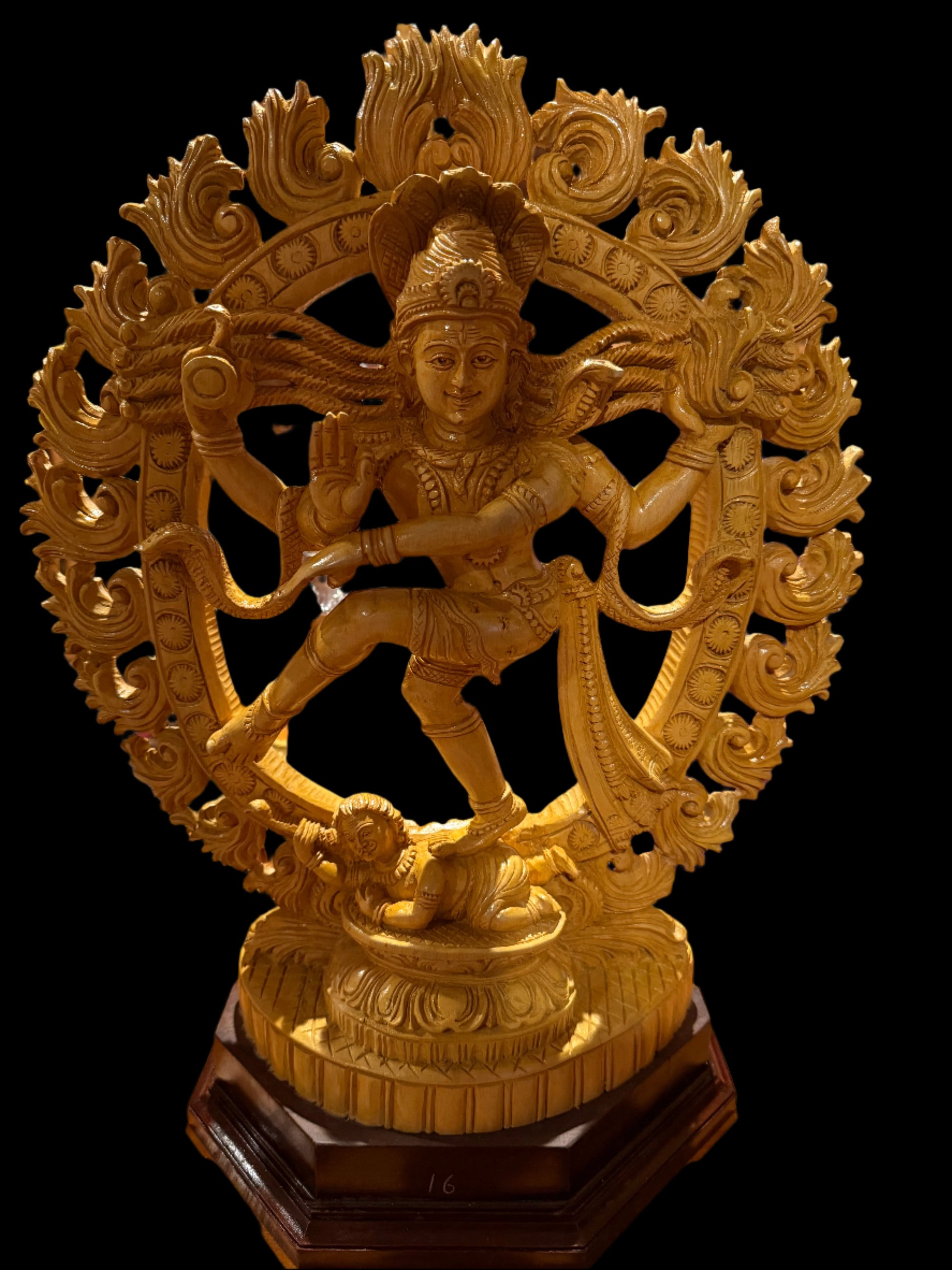 The "Wood Nataraja 20 inch" by Saanskrityam Handicraft Store is a handmade golden statue of a dancing figure, possibly Lord Shiva as Nataraja. The collectible piece features an intricate ornamental halo and stands elegantly on a circular base atop a dark wooden pedestal.