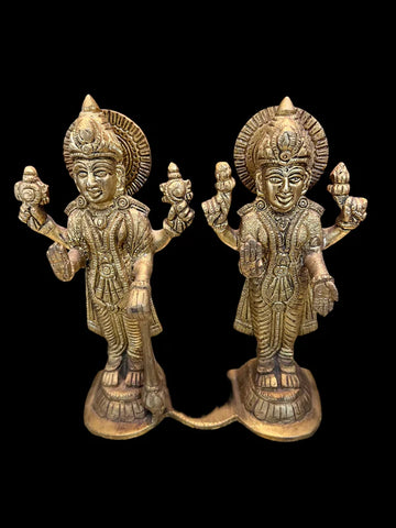 Two identical LakshmiNarayana 6 inch bronze statues from Saanskrityam Handicraft Store, each depicting Indian deities with four arms holding flowers and other objects, are displayed side by side against a black background. The figures are adorned with ornate headdresses and traditional attire.