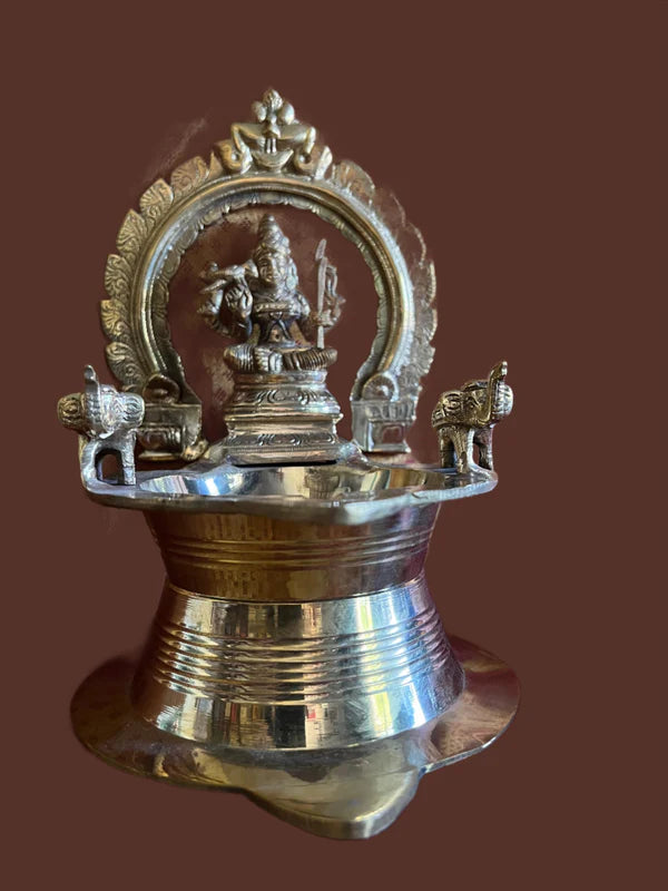 Large Kamakshi lamp crafted in bronze by Saanskrityam Handicraft Store showcases exquisite engravings, featuring a deity figure at its center, flanked by two decorative peacock designs on either side. The lamp boasts a shiny, polished finish against a plain background.