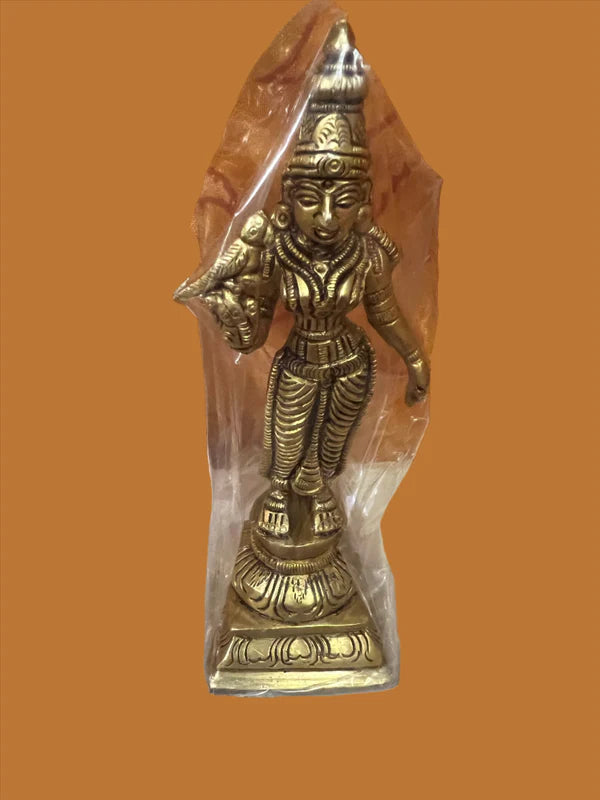 The Saanskrityam Handicraft Store offers a 6-inch Meenakshi bronze statue, depicting the Hindu deity with ornate attire and a conch shell in hand, standing on a decorative base and wrapped in plastic against an orange background.