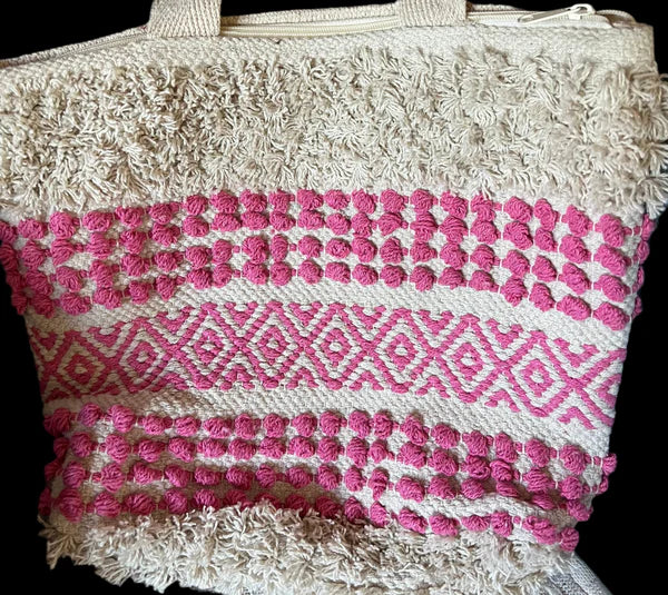 The Multipurpose Handcrafted Bag for a Lady by Saanskrityam Handicraft Store showcases intricate pink geometric patterns on a cream canvas, adorned with rows of pink pom-poms and diamond shapes for a unique textured appearance.