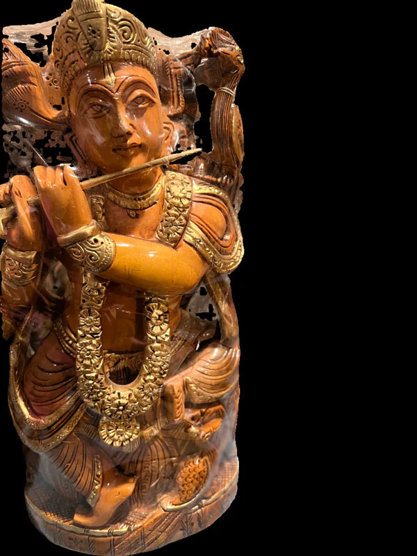 Product Description: The Shisham wood seated Krishna by Saanskrityam Handicraft Store is a meticulously crafted sculpture of the deity Krishna playing a flute. The piece is adorned with elaborate carvings and intricate ornaments, set against a black background. It beautifully captures Krishna in flowing garments and with a serene expression.