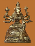 A brass statue named Varaahi Devi 5 inch by Saanskrityam Handicraft Store features a multi-armed deity with a unique headdress, seated cross-legged on an intricately carved base against a plain brown background.