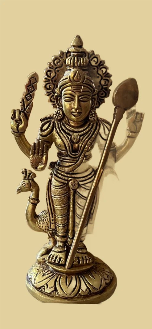 A bronze statue called "With trisoolam or vel" from Saanskrityam Handicraft Store features a four-armed Hindu deity holding various objects, adorned with intricate jewelry and a crown, standing on a lotus pedestal with a peacock at the base.