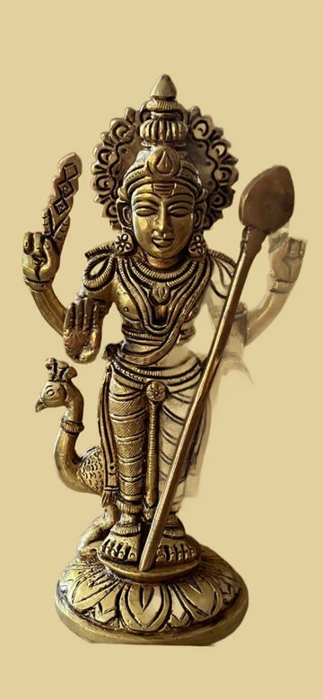 A bronze statue called "With trisoolam or vel" from Saanskrityam Handicraft Store features a four-armed Hindu deity holding various objects, adorned with intricate jewelry and a crown, standing on a lotus pedestal with a peacock at the base.