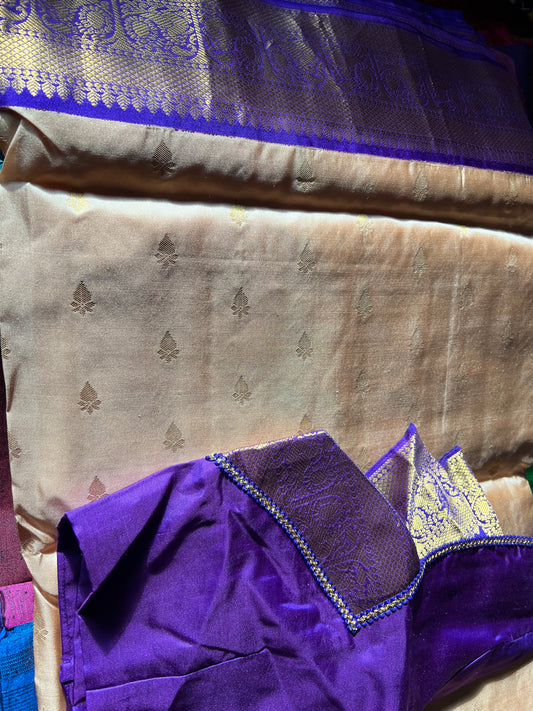 A close-up of the luxurious Kanchipuram silk saree from Saanskrityam Handicraft Store showcases an elegant purple section with intricate gold patterns, paired with a silver section adorned with delicate gold motifs. The pure silk fabric reflects light beautifully, emphasizing its exquisite texture and detailed design typical of high-quality silk sarees.